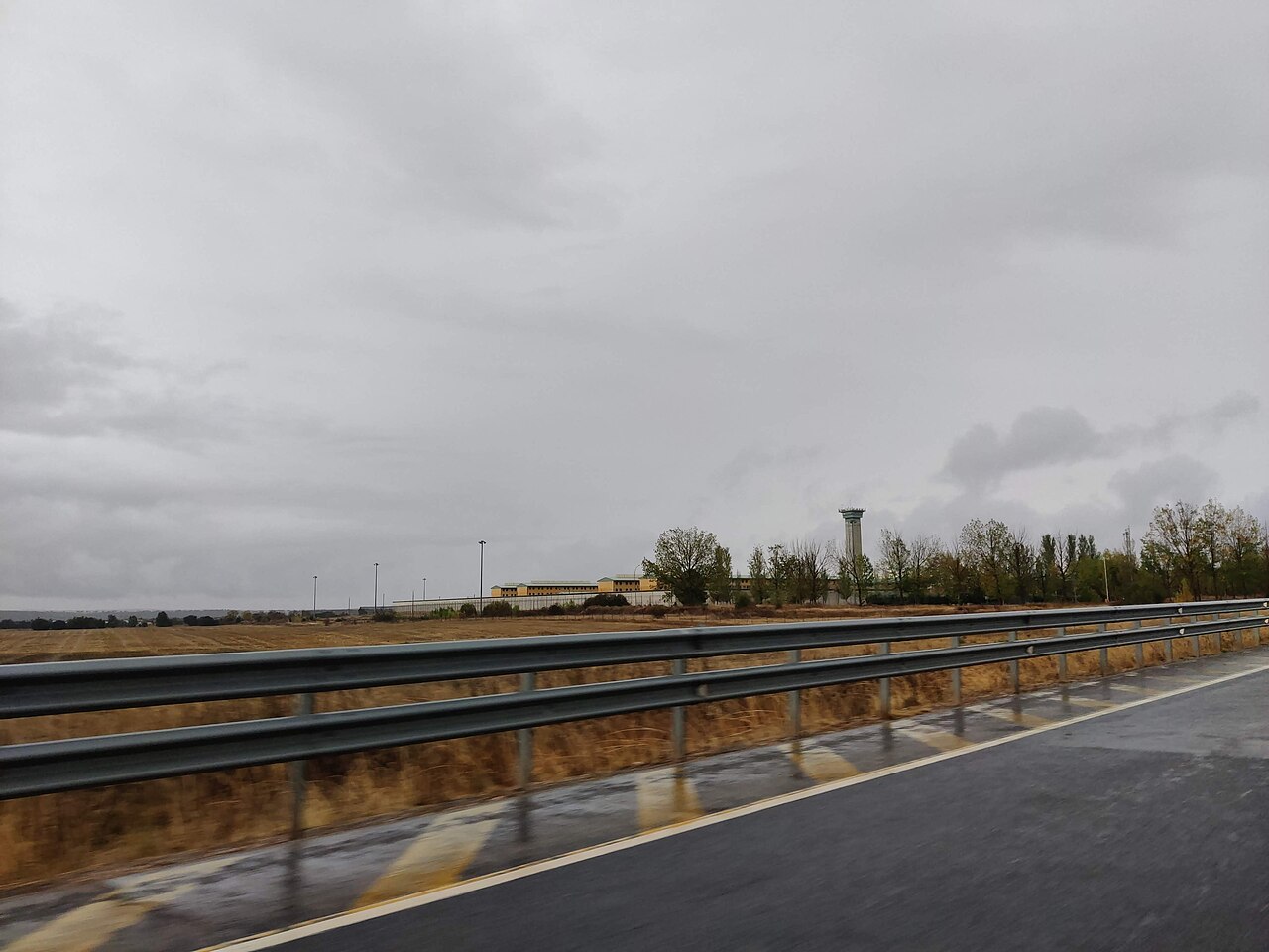 Vista del Centro Penitenciario de Topas (Salamanca) desde la carretera, con el cerramiento perimetral y una torre de vigilancia al fondo bajo un cielo nublado
