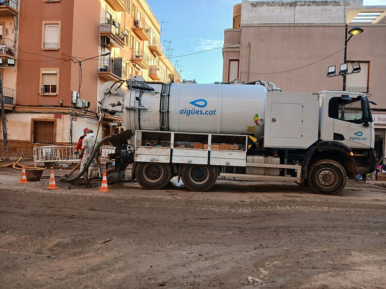 Calle de Paiporta cubierta de barro tras la DANA de 2024, con un camión cisterna de limpieza junto a edificios de viviendas