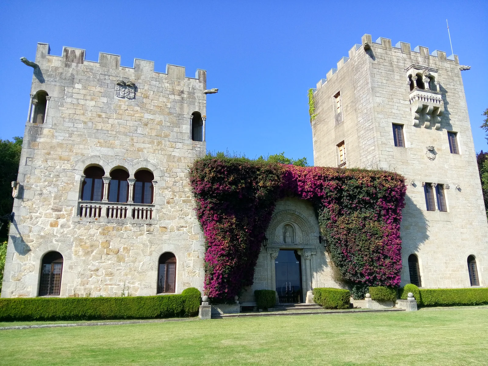 Fachada principal del Pazo de Meirás, en Sada (A Coruña), con sus dos torres almenadas de piedra y una buganvilla en flor sobre la portada de entrada